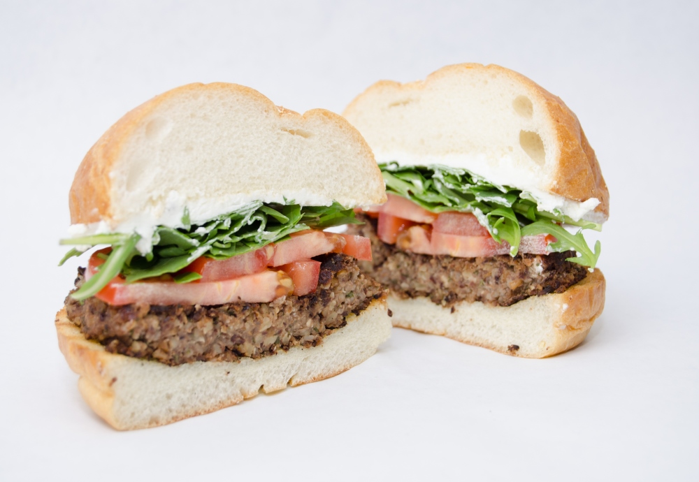 A vegetarian burger with tomatoes, lettuce, and mayonnaise on a fluffy white bun.